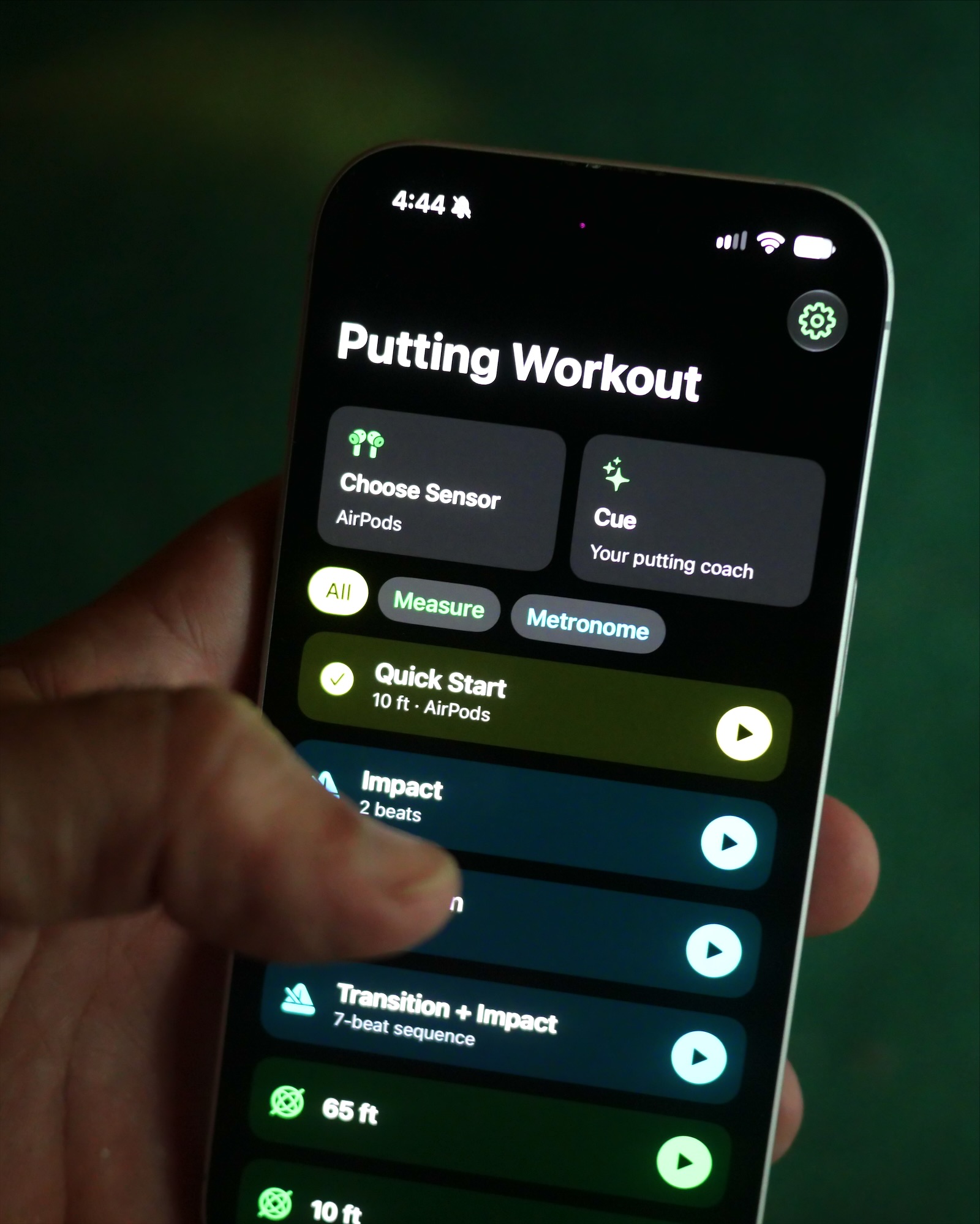 A hand holding an iPhone with the Putting Workout home screen over a green.