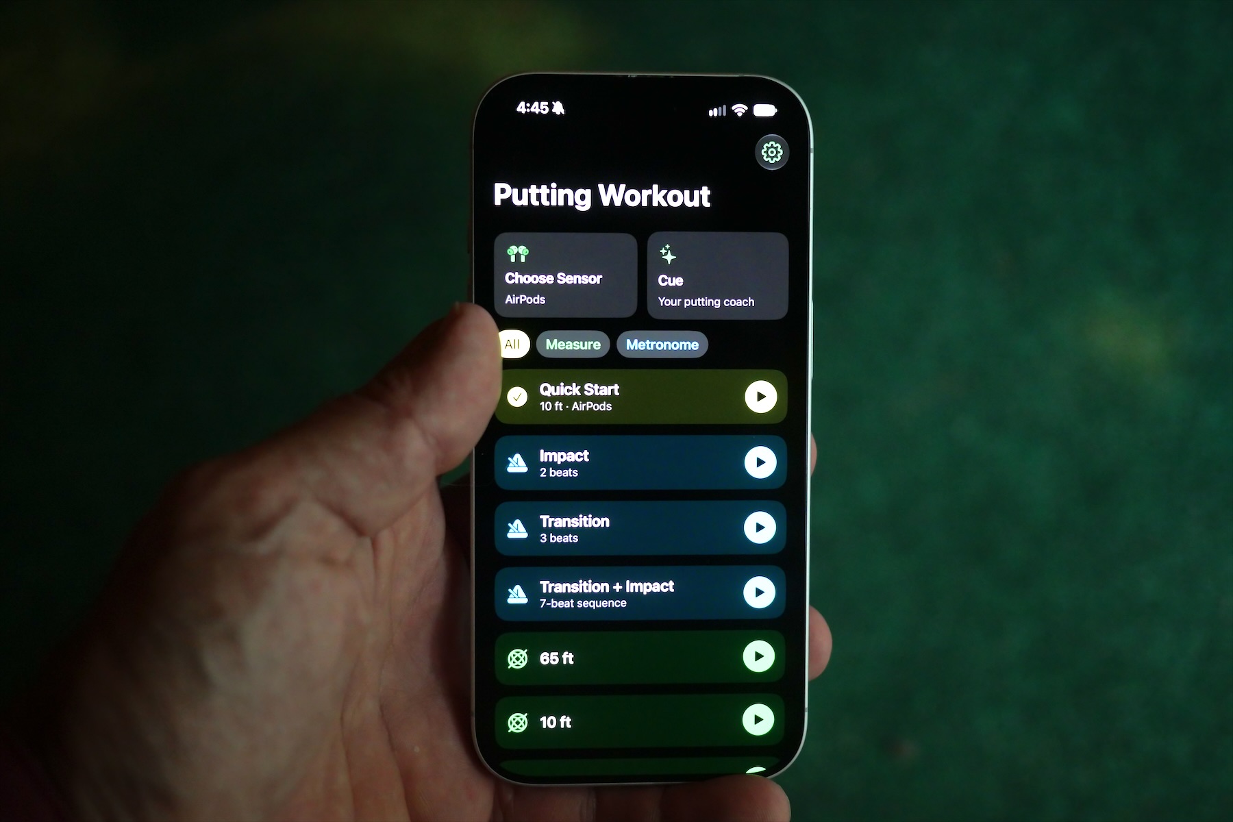 An iPhone held over a practice green, showing the Putting Workout home screen: Quick Start, three metronome modes and measure distances.